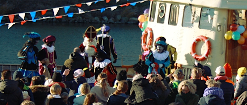 Sinterklaas zelf omringt door vele Pieten zet voet aan wal.