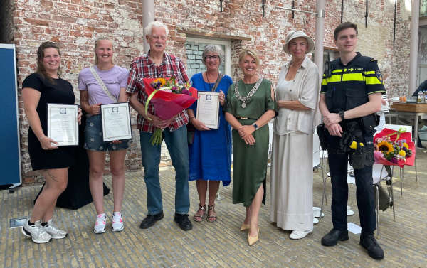 Op de foto staan redders Fleur Roos, Christina Benniks en Klazien Veenstra samen met burgemeester Jannewietske de Vries, politieagent Kris de Weerd, Secretaris van de KMRD Anneke Westerman en met bloemen de geredde meneer Catharinus van der Meer uit Scharnegoutum. Ilse van der Veen kon helaas niet bij de uitreiking aanwezig zijn en ontbreekt op de foto.